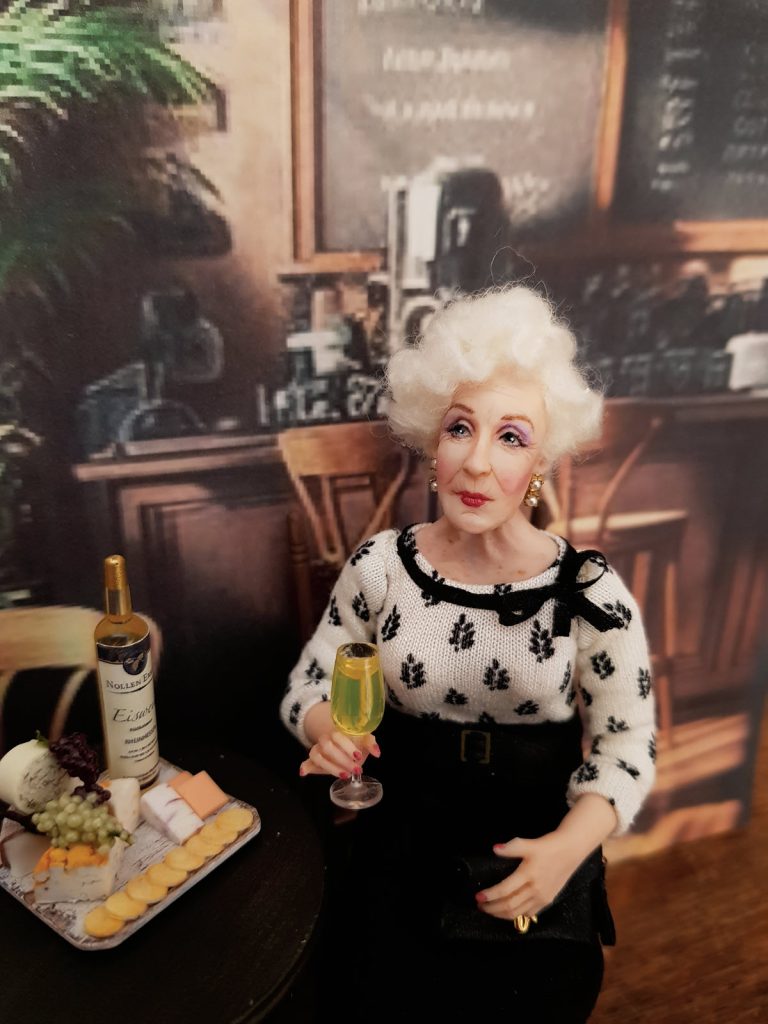 miniatare doll elderly lady in black and white at bar with wine