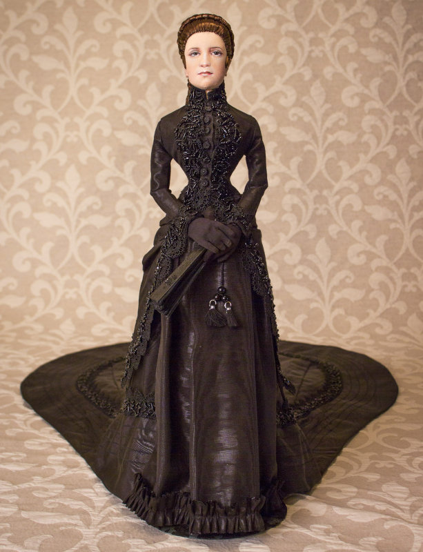 Empress Elizabeth of Austria lived from 1837 to 1898. Wray’s 24-inch OOAK cloth depiction is jointed at the shoulders, upper arms, hands, wrists, hips, knees, and ankles. She wears authentic silk underclothes, undershirt, and breeches, a functional corset, bustle, and petticoat. Her jacket skirt is made from black watermarked fabric trimmed in black lace and heavily hand-beaded trim. She wears low-heeled slippers with beaded bows and carries a handmade hand fan.