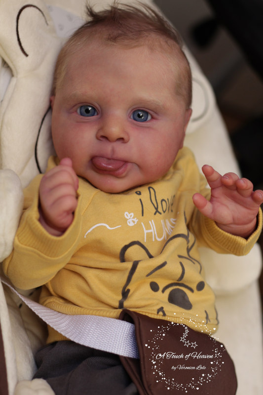 Realistic baby doll looking at the camera, with his tongue sticking out a bit.